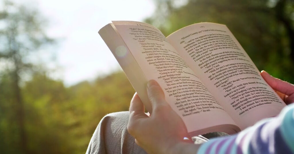 A person reading "A Quick and Easy Guide to Choosing Which Book of the Bible to Read" while sitting in a serene park.