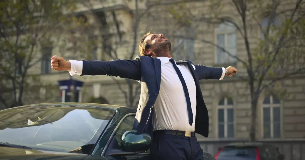 A man in a suit stands confidently on the hood of his car, symbolizing the theme of Successfully Launching Your Work.