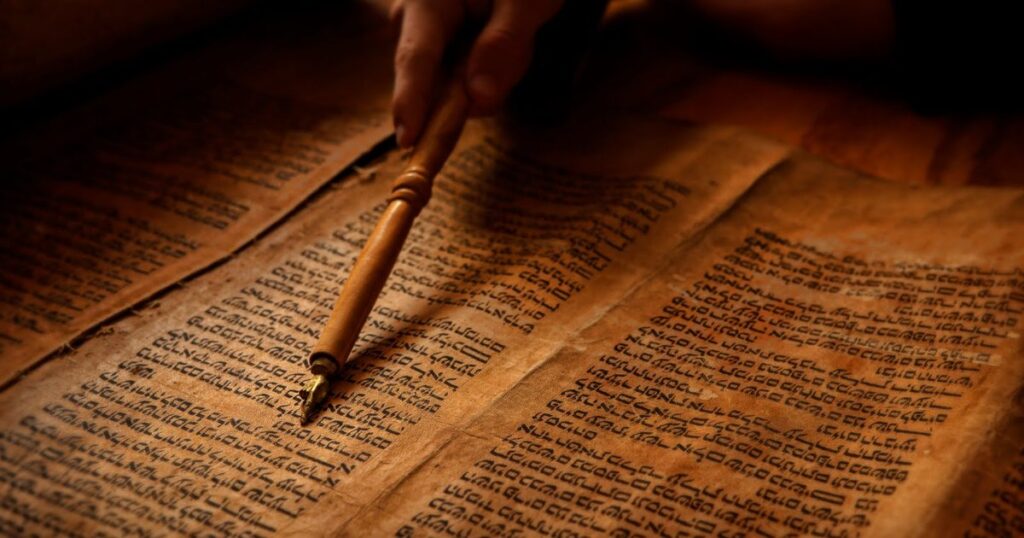 A person holding a pen above an open book of the law, symbolizing the study of The Hebrew Bible and its teachings.