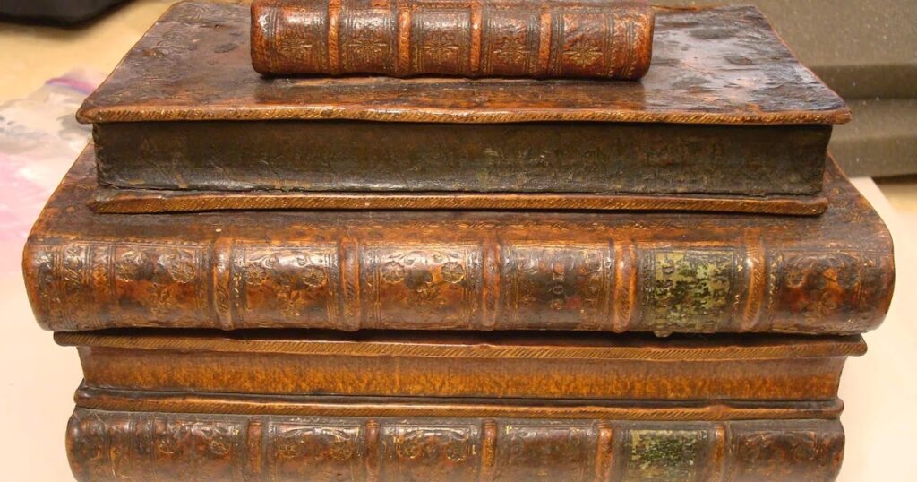 A stack of historical books resting on a wooden table, showcasing their aged covers and worn spines.