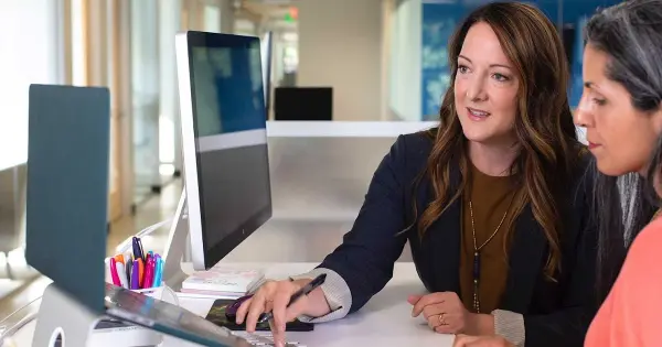 Two women collaborate on a computer, exploring options to self-publish by hiring a service company.