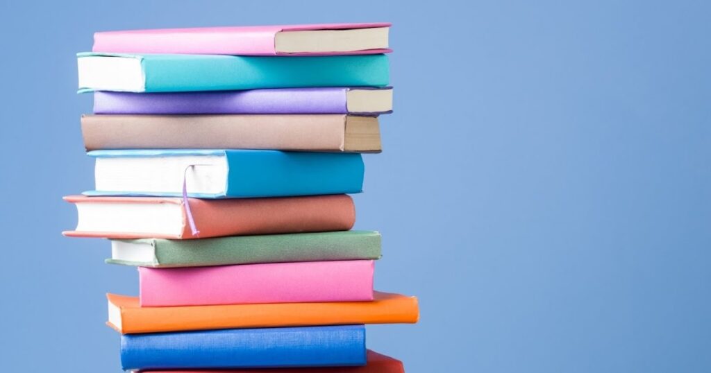 A stack of books on a blue background, symbolizing the journey of self-publishing: "How Long Does it Take to Self-Publish a Book.