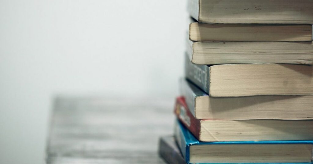 A stack of books on a table, illustrating the question: "How Much is a Book of the Month?" in a cozy reading setting.